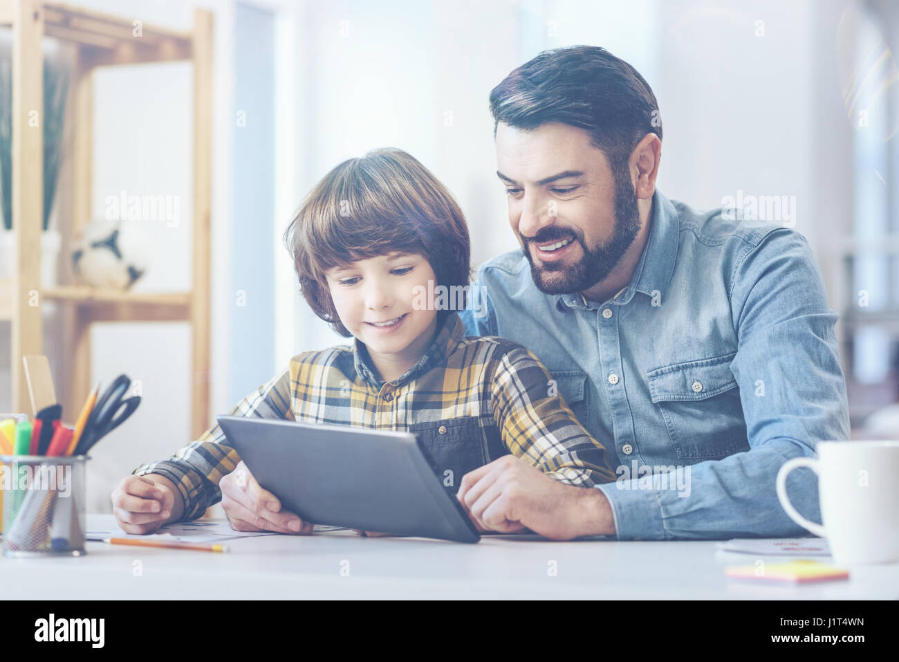 Padre e figlio giocare con tavoletta digitale alla scrivania Foto Stock
