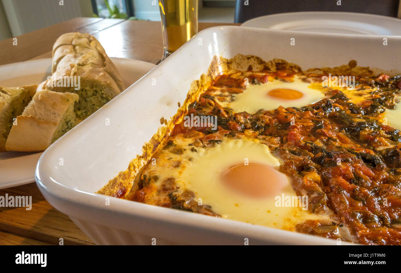 Close up di cosse al forno sgombro affumicato, spinaci, pomodori, lo scalogno e le uova in ceramica bianca teglia con aglio pane, Scotland, Regno Unito Foto Stock