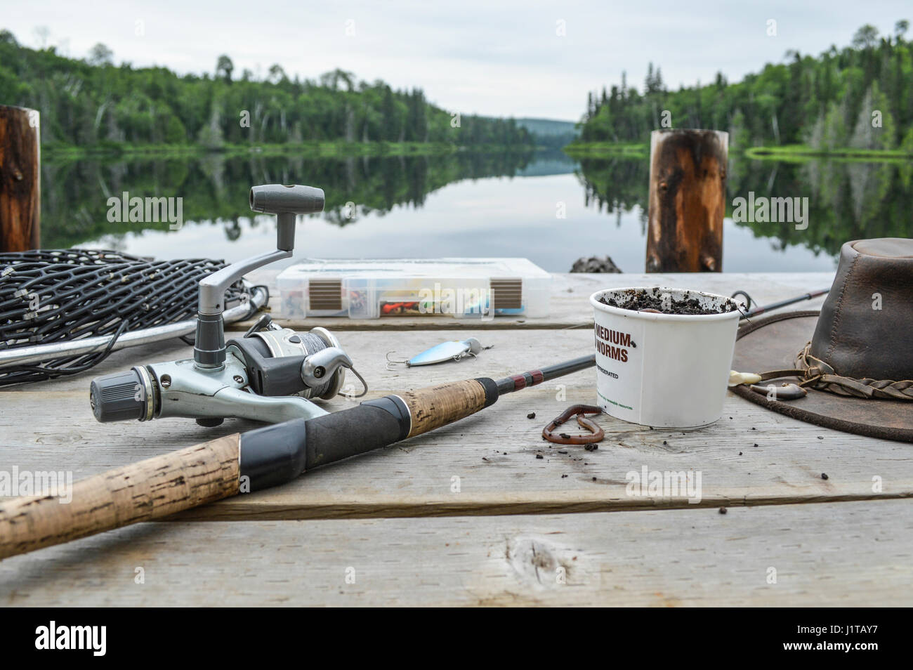 Canna da pesca, scatola di vermi, Cappello in cuoio, alcuni affronta e la rete da pesca sul molo. Foto Stock