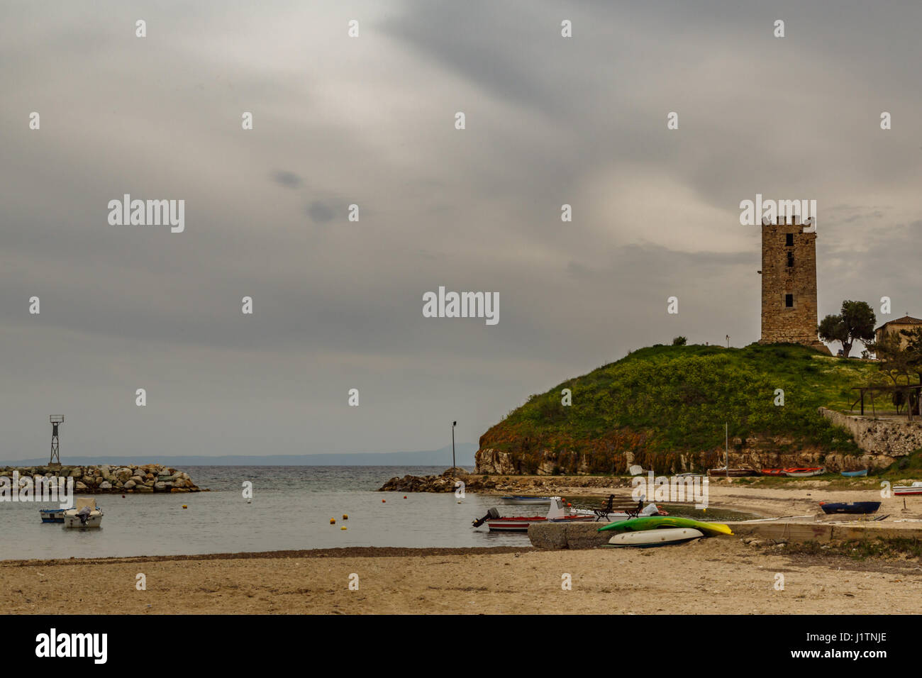 Torre Bizantina su una collina al mare e contro un cielo nuvoloso e la spiaggia con barche, Nea Fokea (Calcidica), Grecia Foto Stock