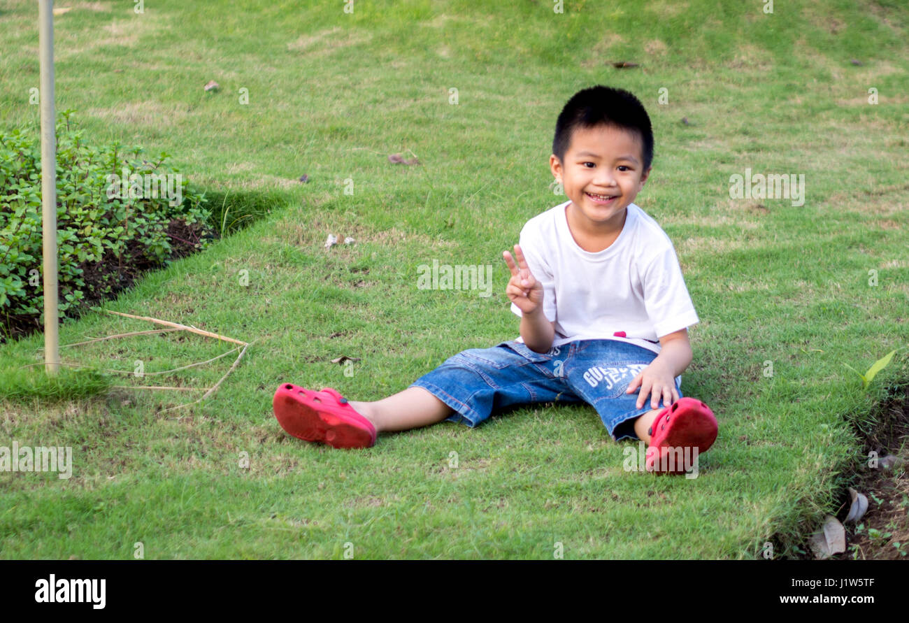 Bambino cinese (boy) Sedersi sull'erba Foto Stock