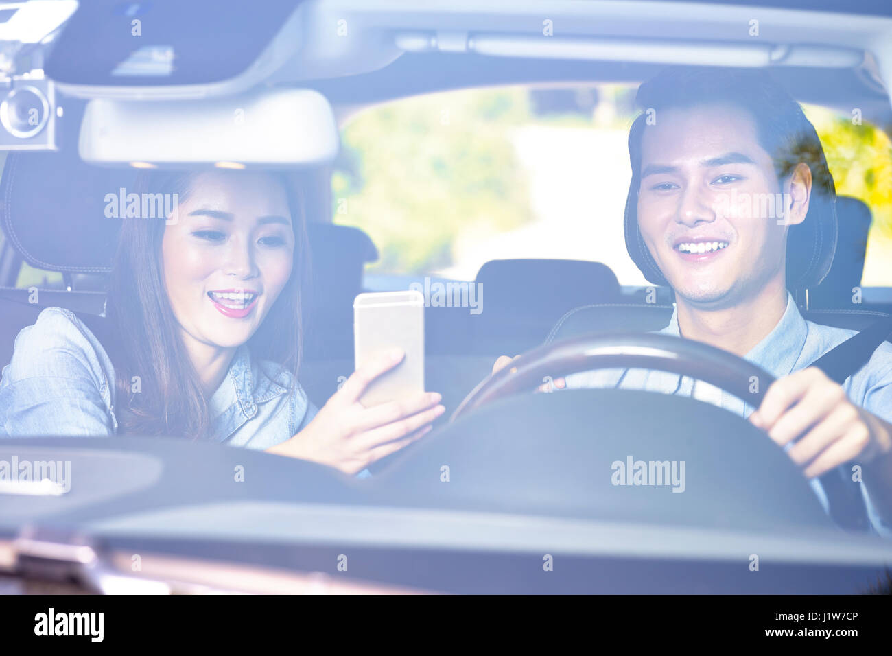 Felice giovani asiatici giovane utilizzando il cellulare per navigare durante la guida di un'auto. Foto Stock