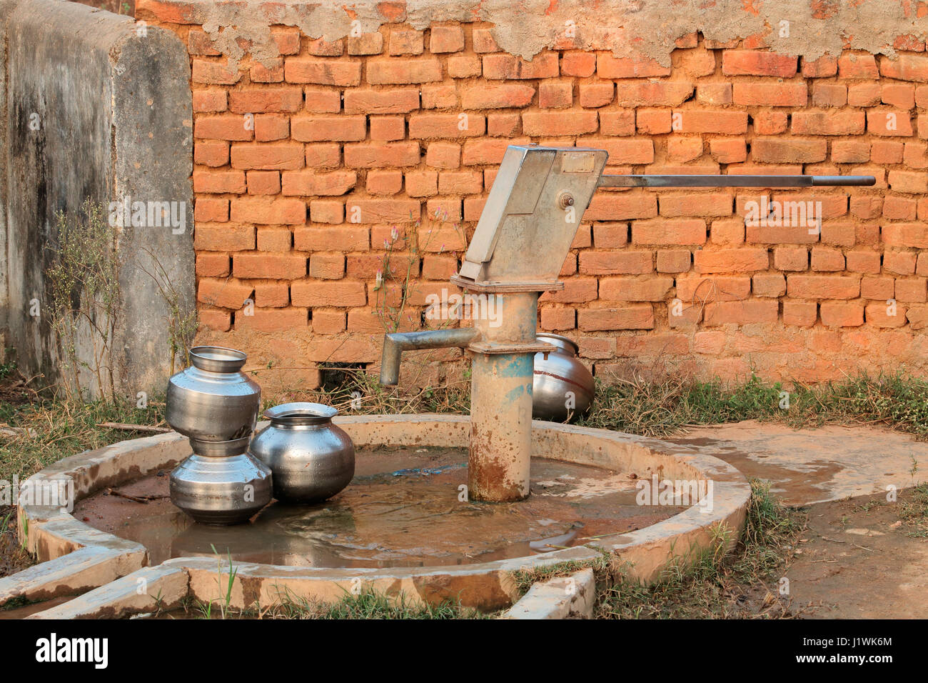 Vecchio azionato a mano la pompa acqua e contenitori di acqua in India rurale Foto Stock