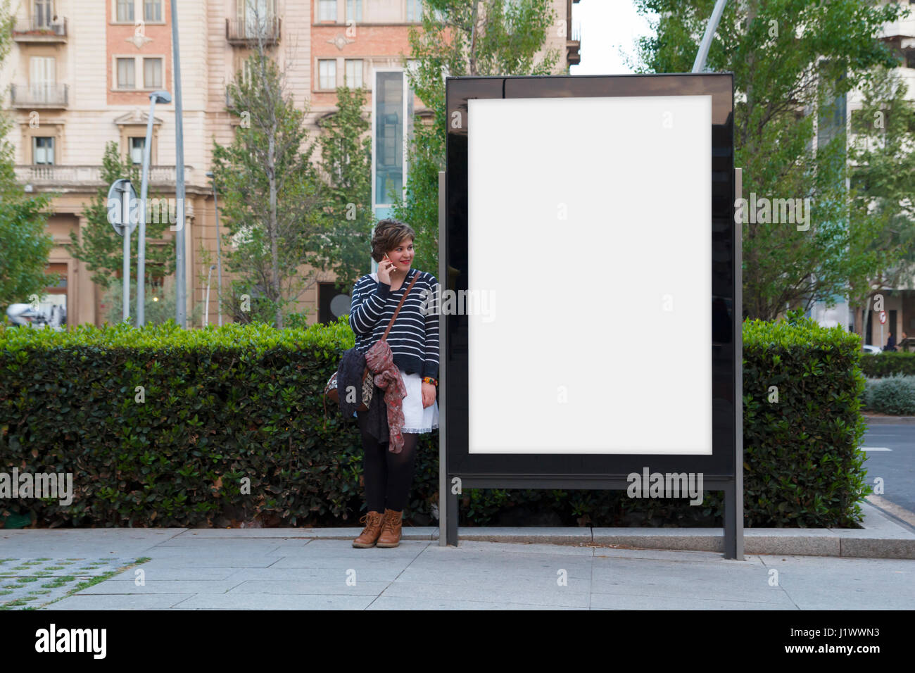 Donna che parla con il telefono cellulare e in piedi in un tabellone vuoto Foto Stock