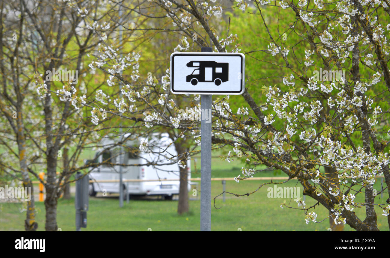 Zeichen, Schild für Wohnmobil-Stellplatz, im Hintergrund hinter Bäumen blühenden ein Reisemobil; RV dietro il simbolo di parcheggio e struttura di fioritura Foto Stock
