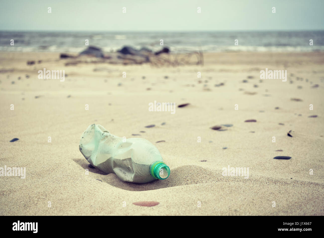Retrò immagine stilizzata di un vuoto verde bottiglia di plastica a sinistra su una spiaggia, il fuoco selettivo, inquinamento ambientale concetto immagine. Foto Stock