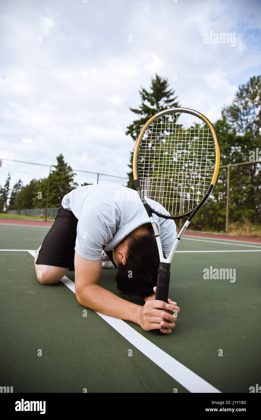 Un triste asian giocatore di tennis inginocchiati in delusione dopo la sconfitta Foto Stock