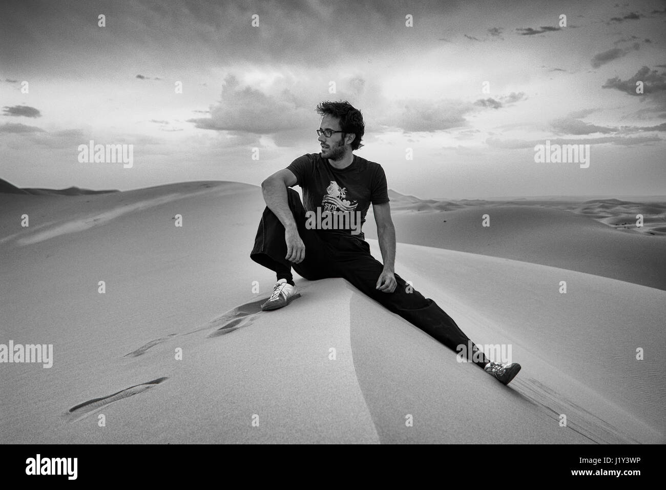 Giovane uomo seduto su una duna nel Sahara marocchino Foto Stock