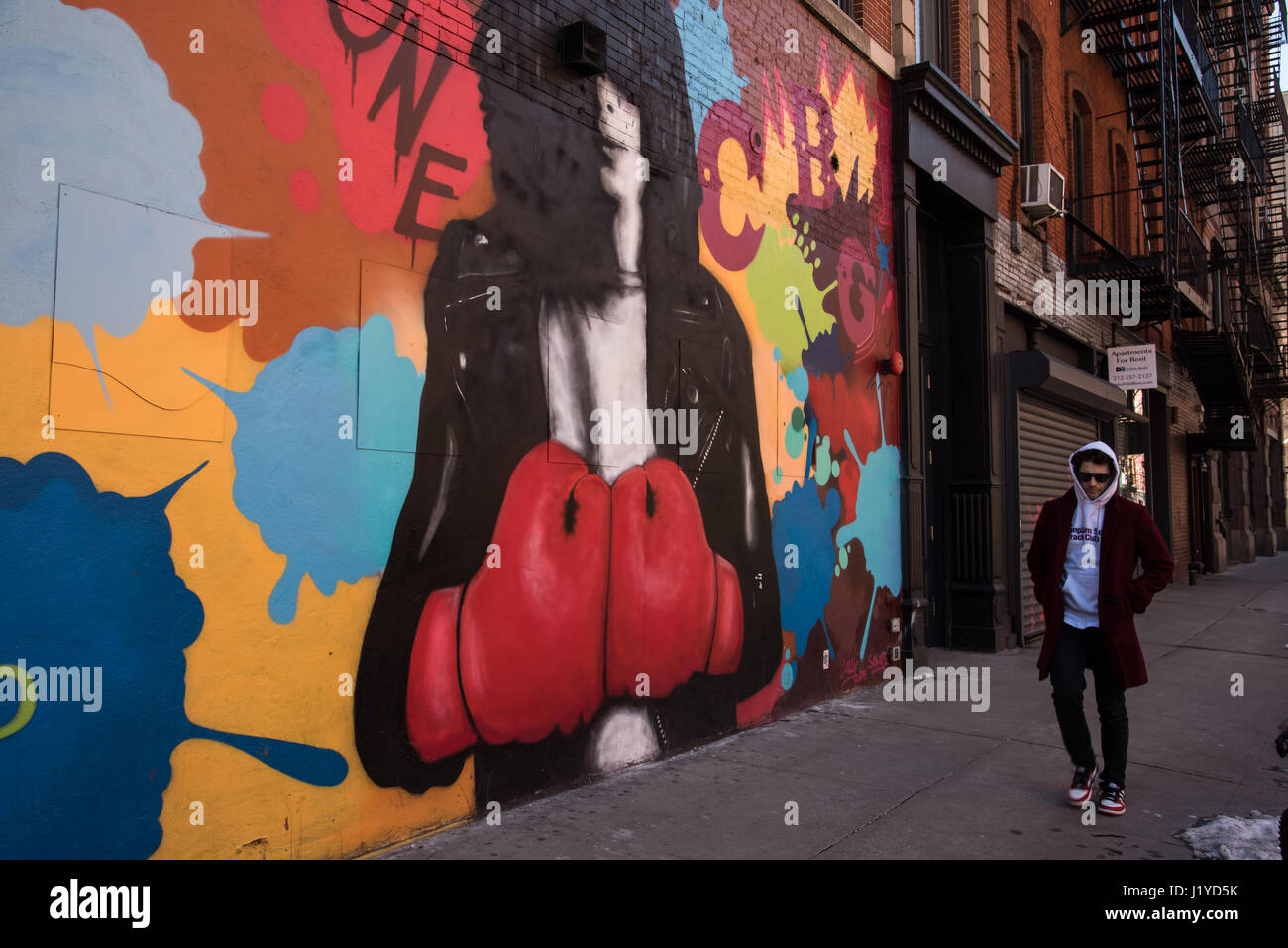 Uomo che cammina davanti un muro di graffiti. Strade di New York City Foto Stock