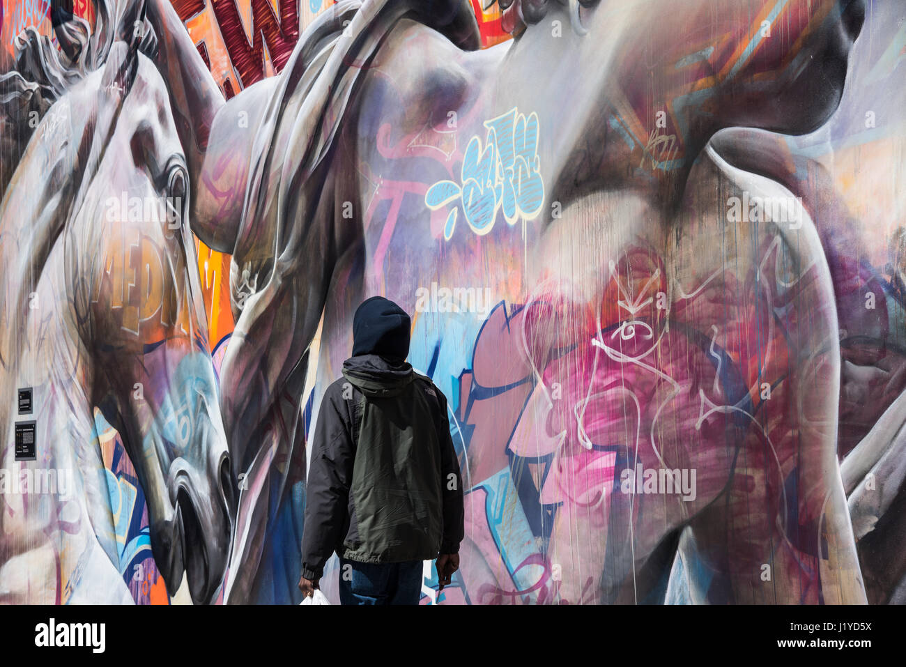 Uomo che cammina davanti un muro di graffiti. Strade di New York City Foto Stock