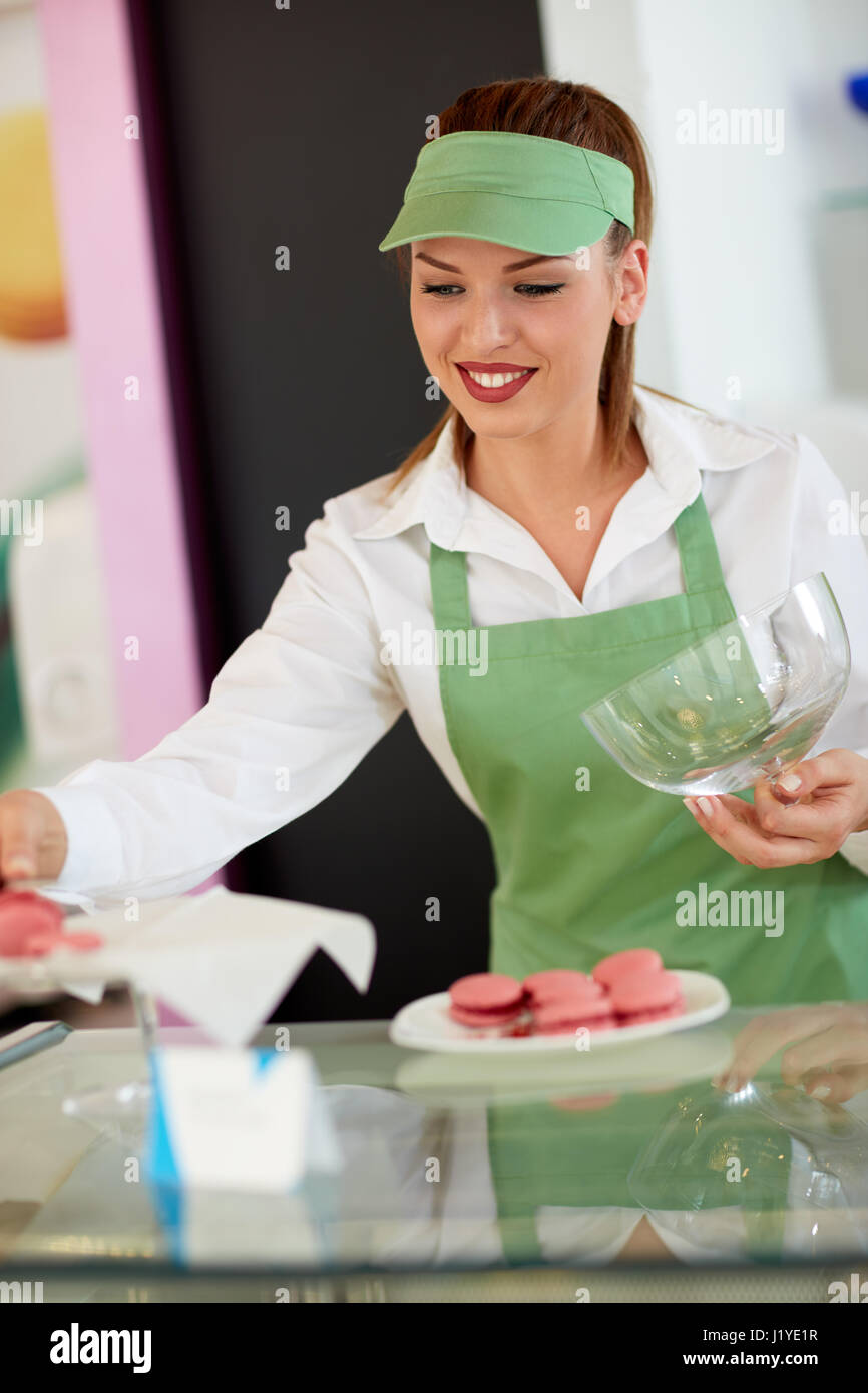 Bella femmina mettendo fornitore macaronis sulla piastra in negozio di pasticceria Foto Stock