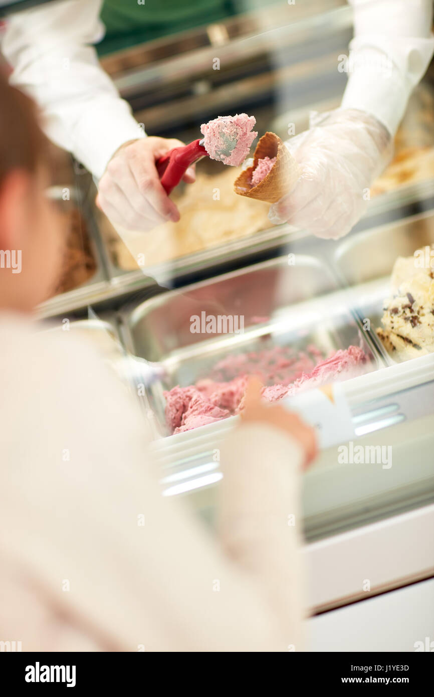 Chiusura del fornitore le mani in pasticceria mettendo gelato sfere in cono Foto Stock