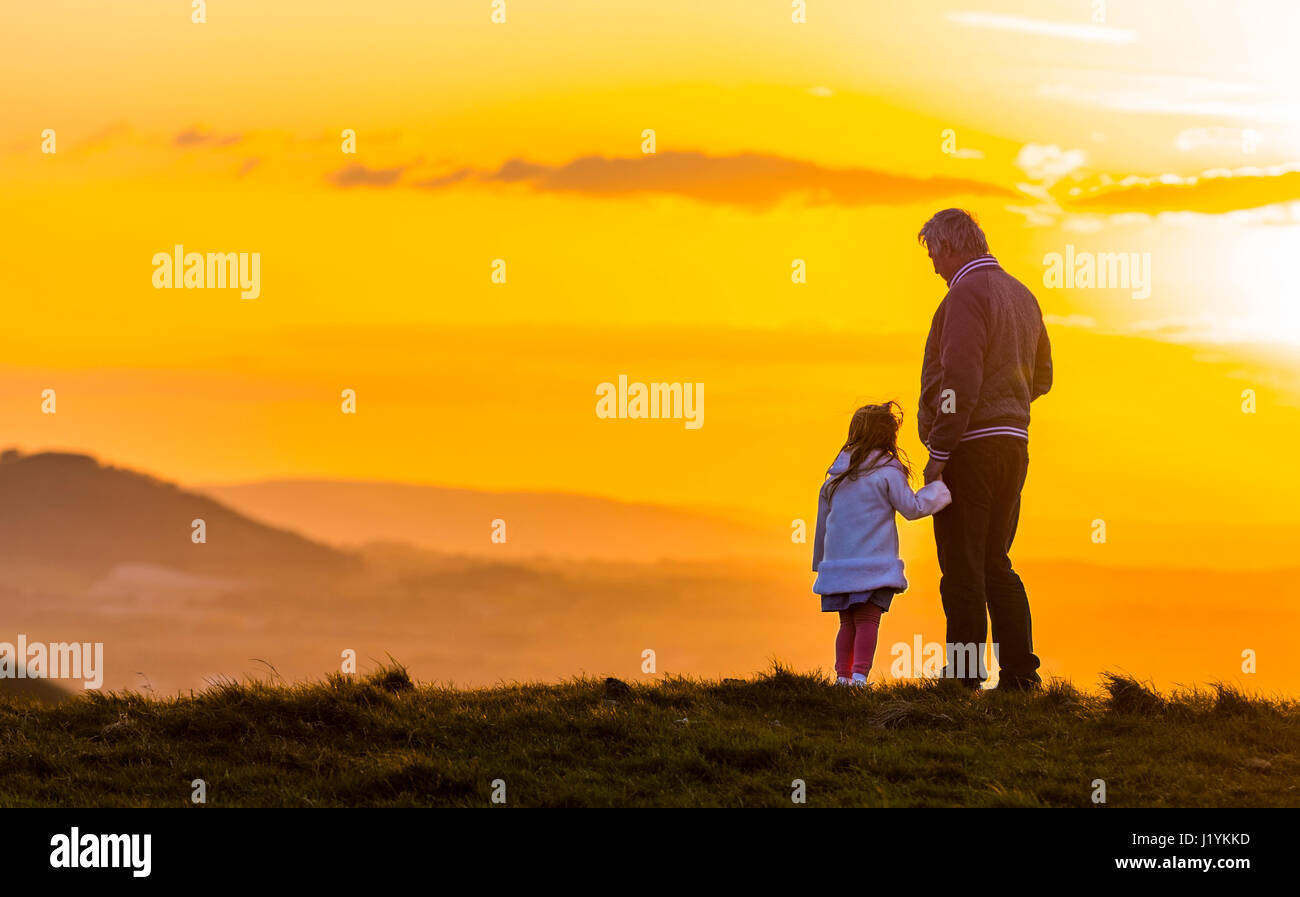 Padre figlia del rapporto. Padre e figlia insieme permanente tenendo le mani su una collina, godendo di guardare il sole andare giù. Foto Stock