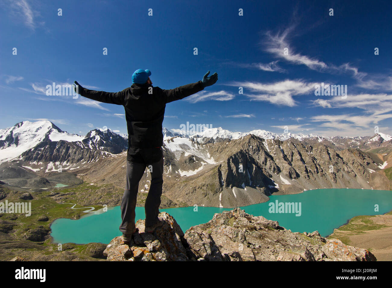 Uomo in camicia nera in piedi con le mani in alto sopra la calma blue mountain lake Alakol con montagne circondate Foto Stock