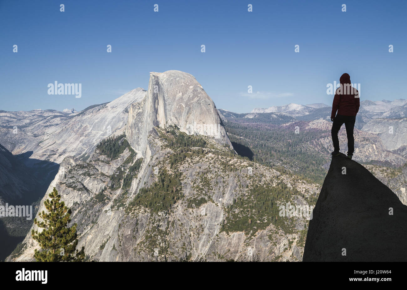 Un giovane escursionista è in piedi su una roccia godendo della vista verso il famoso Half Dome presso il Glacier Point in beautiful Golden luce della sera al tramonto in estate Foto Stock