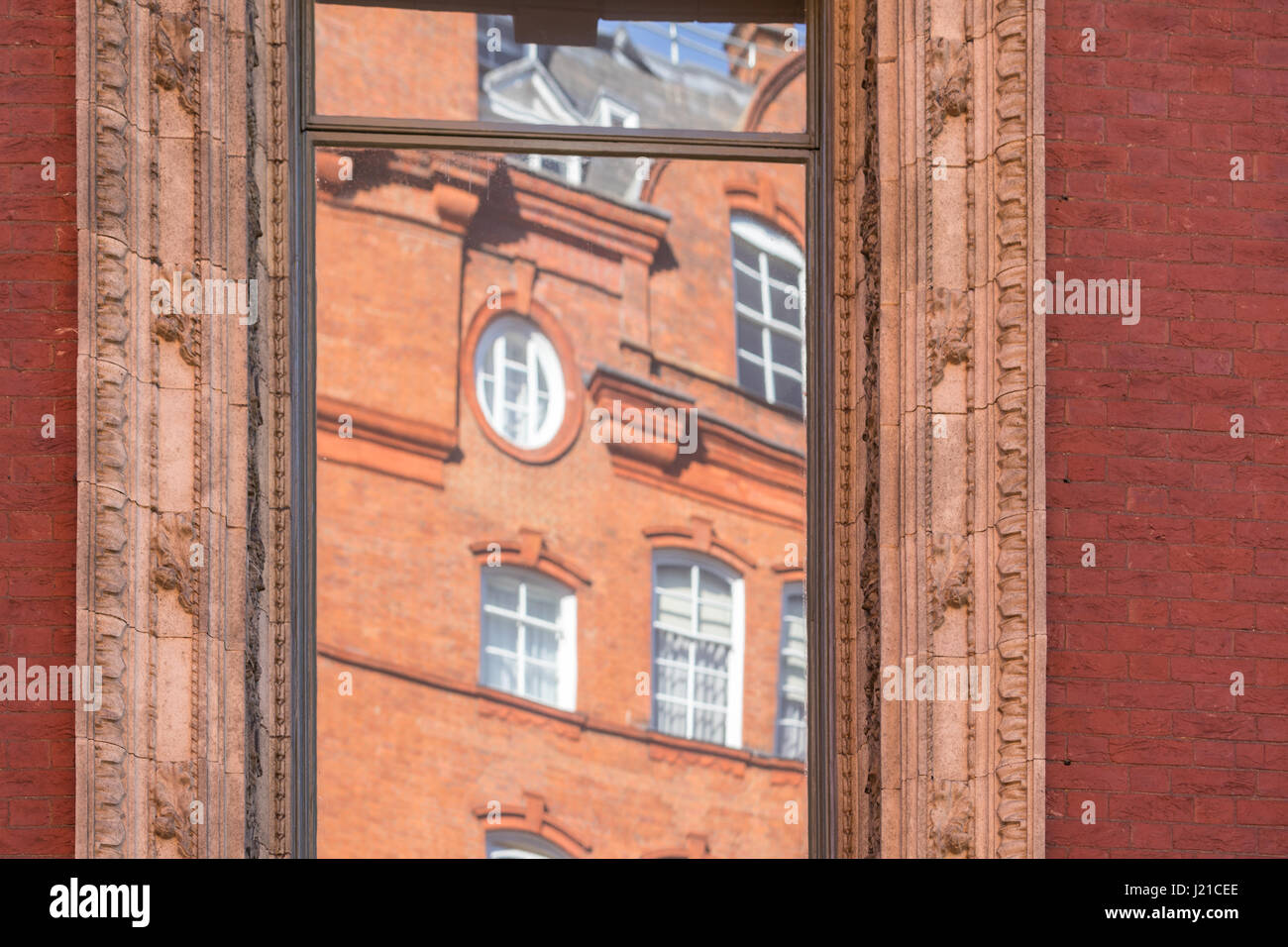 La riflessione di un vecchio edificio in mattoni a Londra in un una finestra con elaborati stampaggio, Londra Inghilterra, Regno Unito Foto Stock