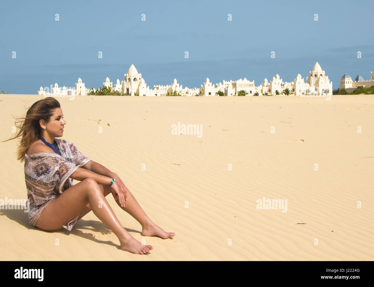 Piuttosto giovani brunette seduto nel deserto con un palazzo sullo sfondo Foto Stock