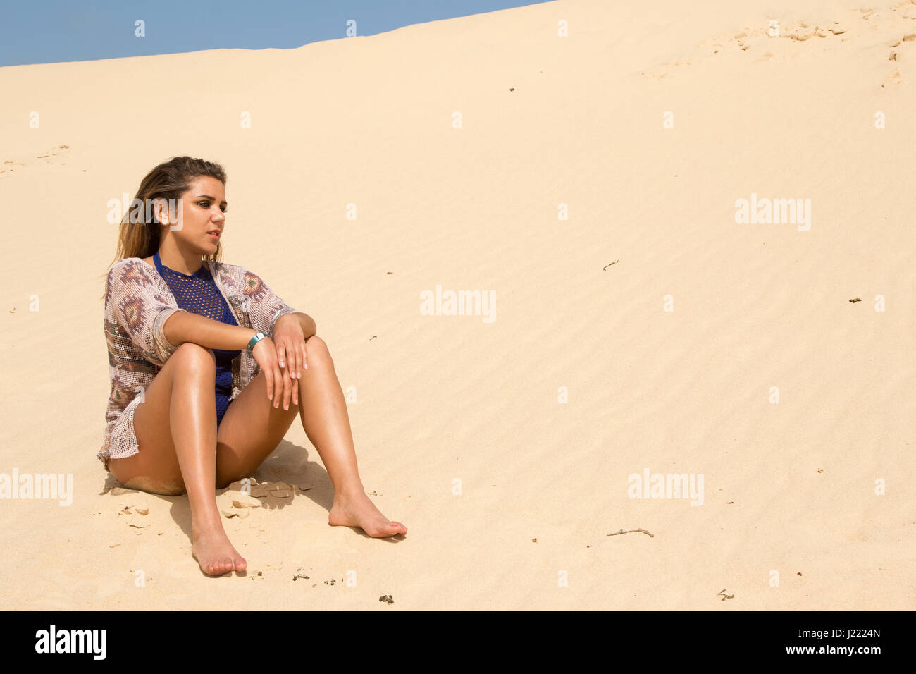 Una donna sola seduta pensando nella sabbia Foto Stock