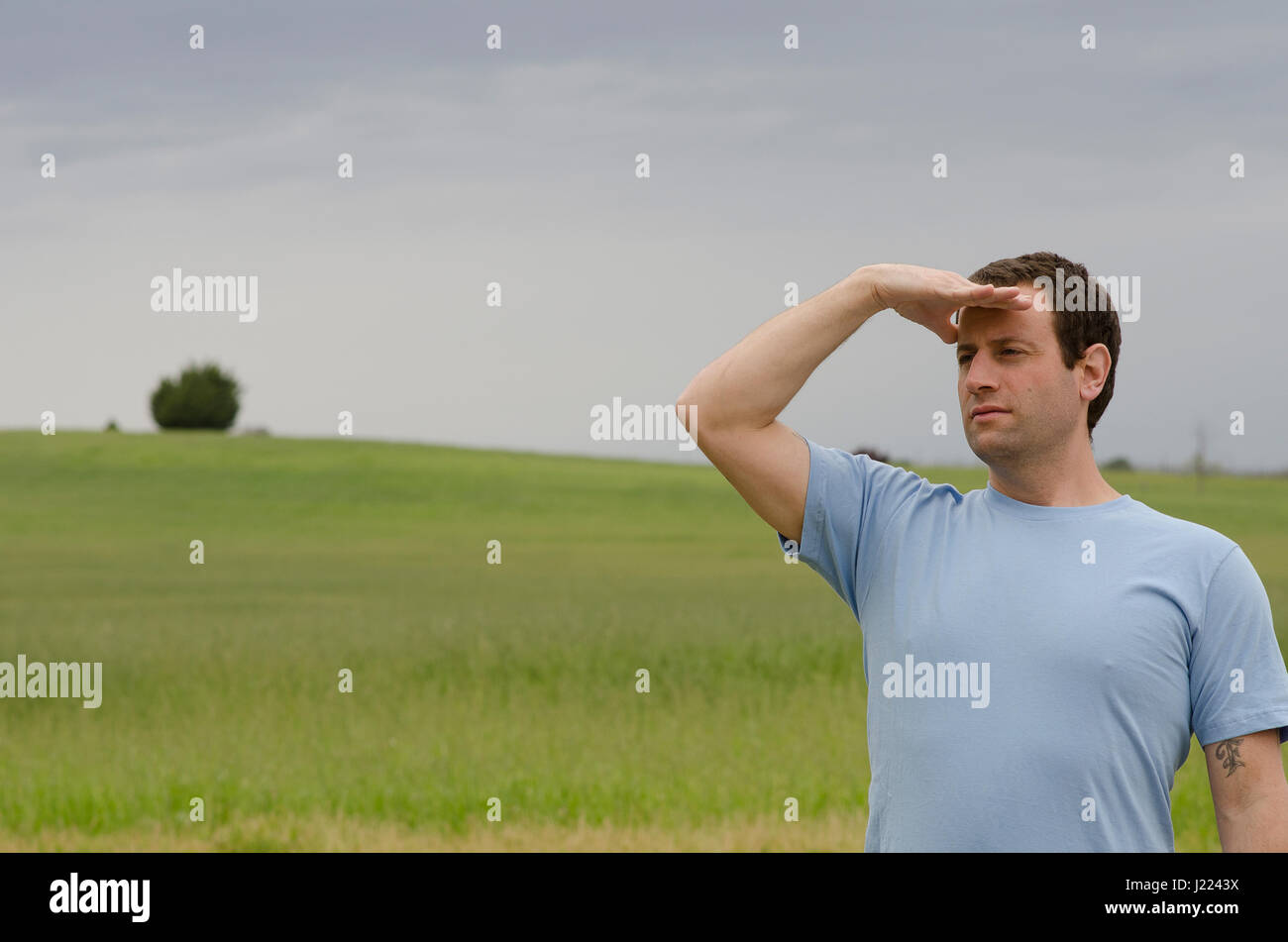 L'uomo con la mano sulla sua fronte guardando fuori nella distanza con un campo erboso in background. Foto Stock