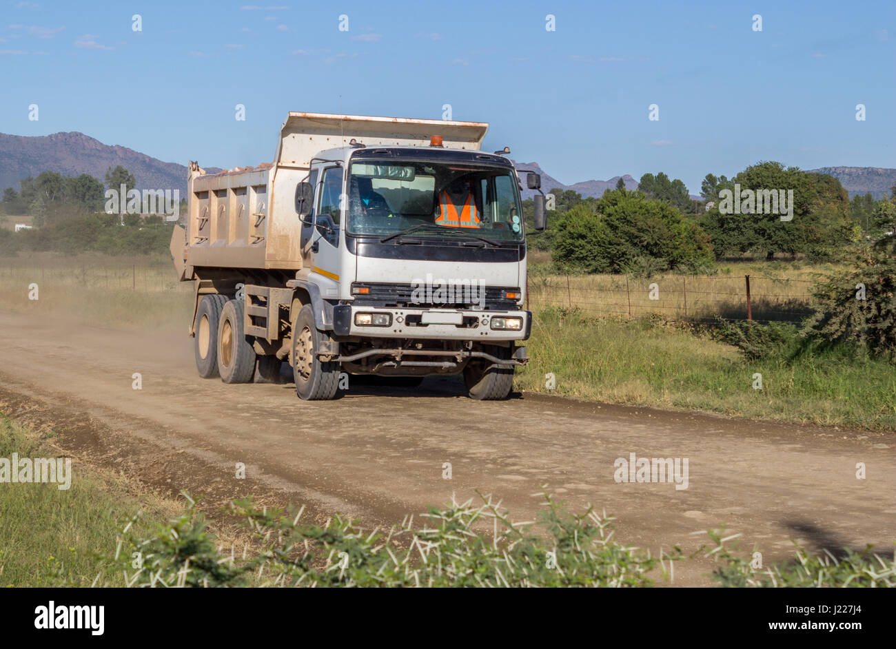 Costruzione bianca carrello in movimento veloce con carico di roccia e sabbia su rurale strada sterrata - fotografia Foto Stock