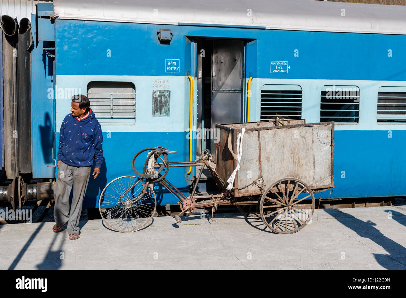 Locale indiana uomo in piedi con un travagliato, usurata triciclo da un carrello ferroviario alla stazione di Kathgodam, distretto di Nainital, Uttarakand, India settentrionale Foto Stock
