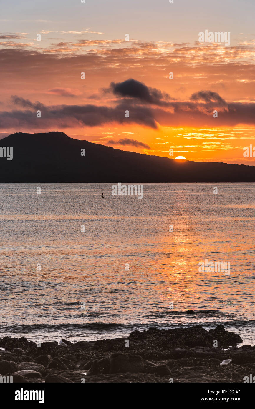 Auckland, Nuova Zelanda - 2 Marzo 2017: Tramonto sul vulcano Rangitoto, girato da Tapapuna spiaggia nel Golfo di Hauraki. Shot 2 di 4. Mezza sun, volc nero Foto Stock