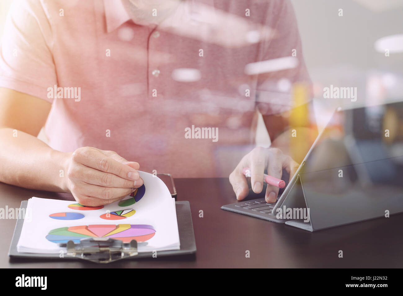 Imprenditore nel t-shirt rosa lavora con digitali computer tablet e apertura del documento sulla scrivania di legno in un ufficio moderno con vetro vista riflessa Foto Stock