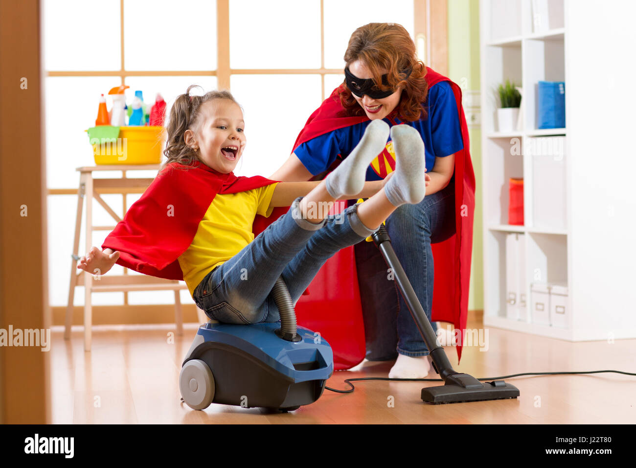 Super Hero kid volare sull'aspirapolvere. La madre e il bambino figlia la pulizia della camera e hanno una divertente Foto Stock