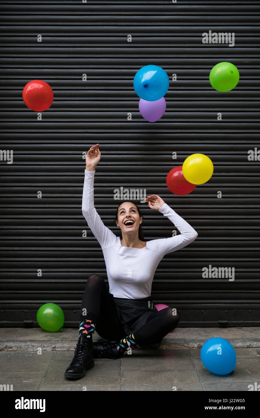 Ridendo giovane donna seduta su un marciapiede guardando battenti palloncini Foto Stock
