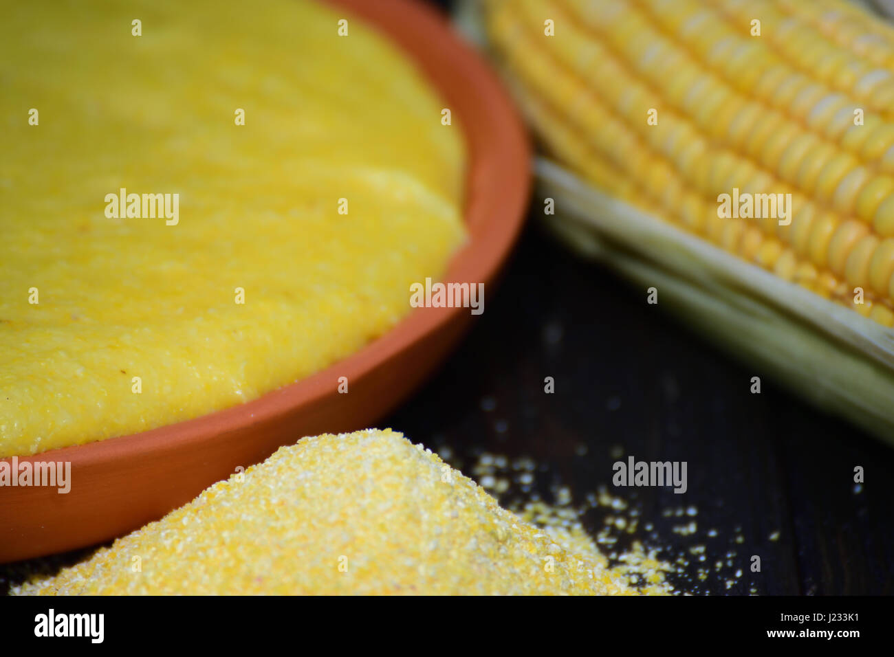 Mucchio di grano macinato, polenta e un tutolo di mais posto su una tavola di legno nella luce naturale Foto Stock