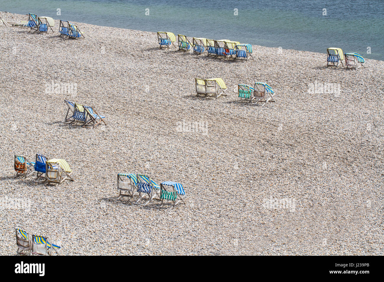 Guardando verso il basso a partire da un angolo alto sulla deserta spiaggia di ghiaia alla birra nel Devon, Regno Unito con vuoto, striped sdraio sparse intorno. Foto Stock