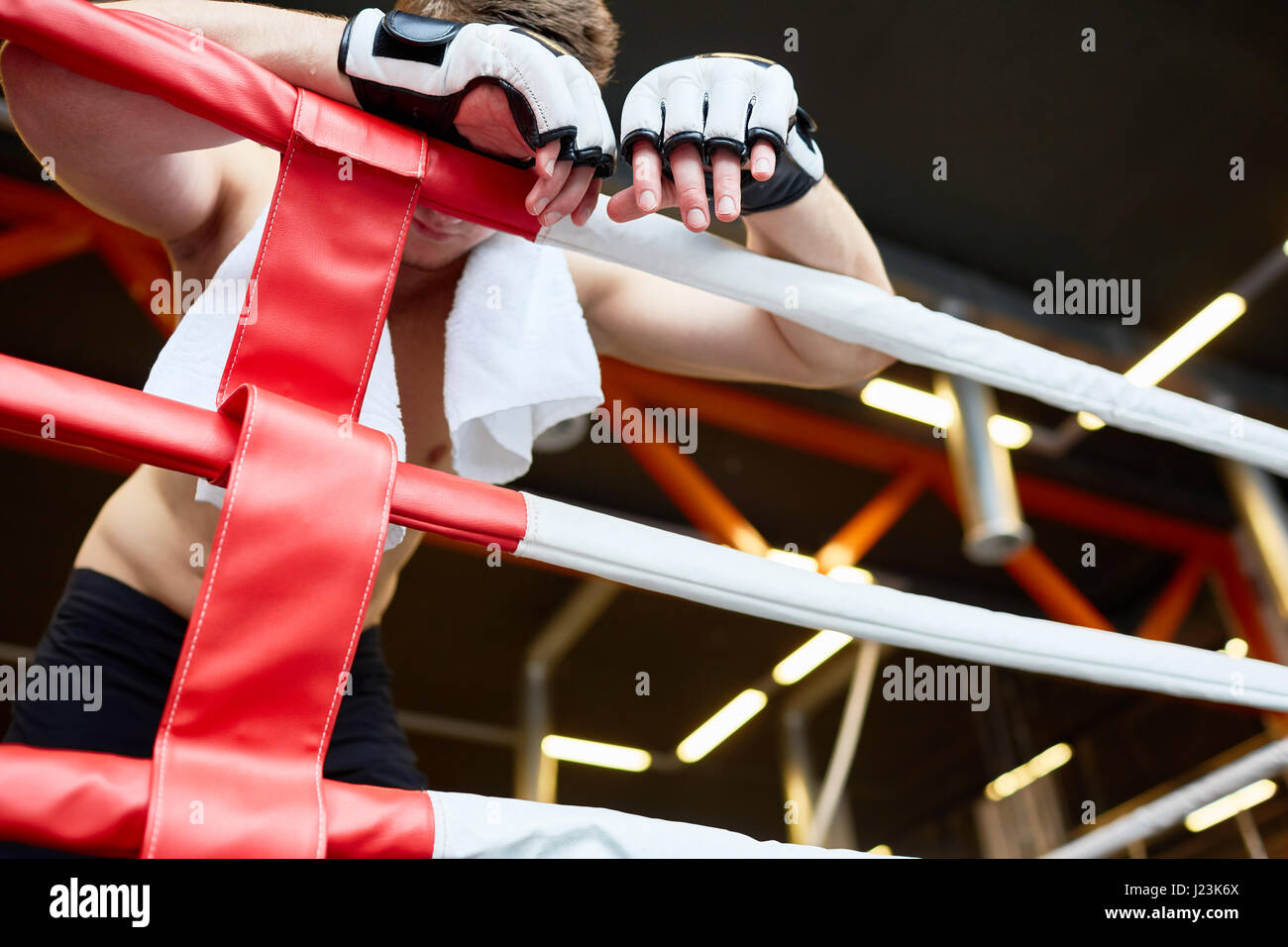 Bassa angolazione del boxer esausto appoggiata sulle funi ad anello con asciugamano sulle spalle dopo dura lotta Foto Stock