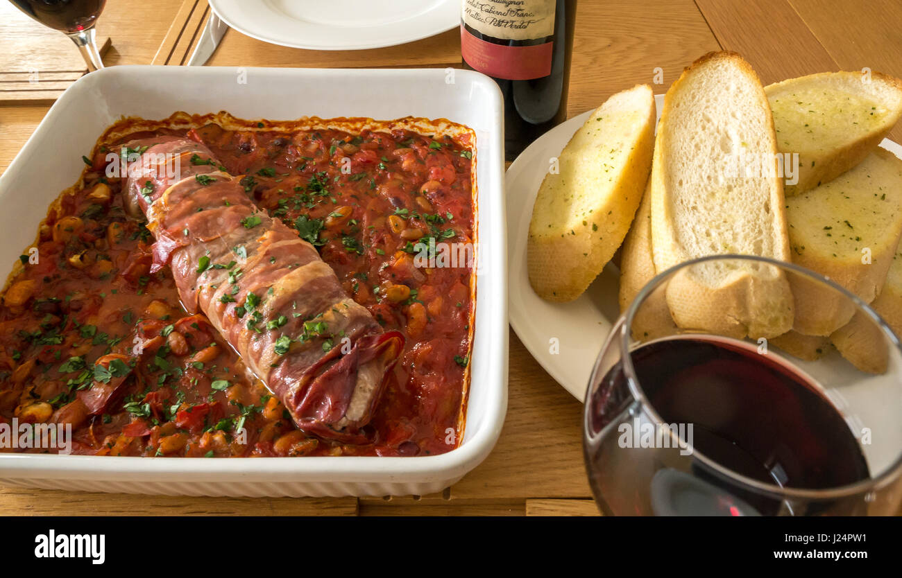 Primo piano filetto di maiale italiano su letto di pomodori, fagioli e aglio con piatto di pane all'aglio, bicchiere di vino rosso Foto Stock