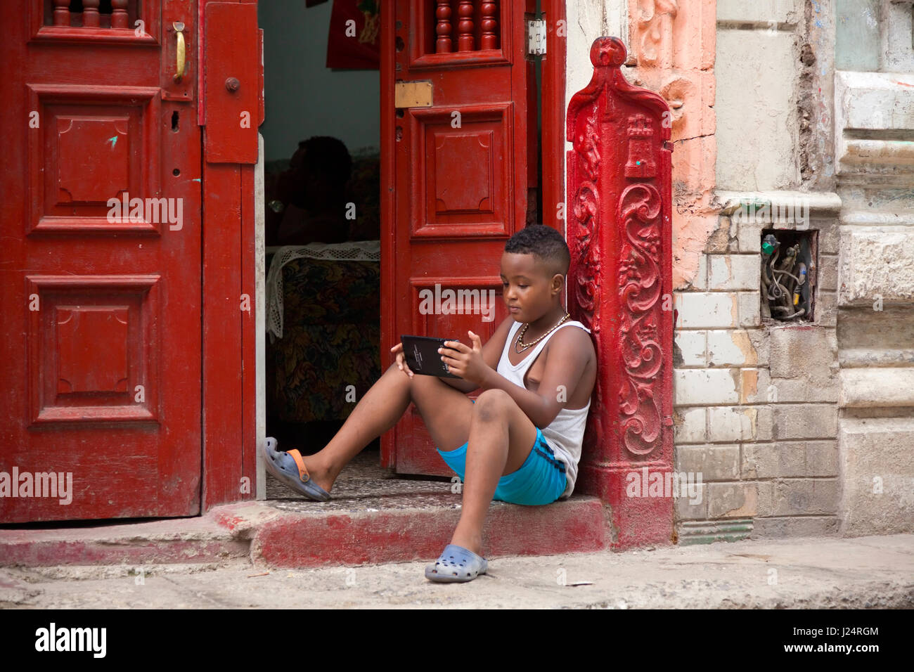 Un bambino di un tablet seduto su una porta di casa a l'Avana, Cuba. Foto Stock