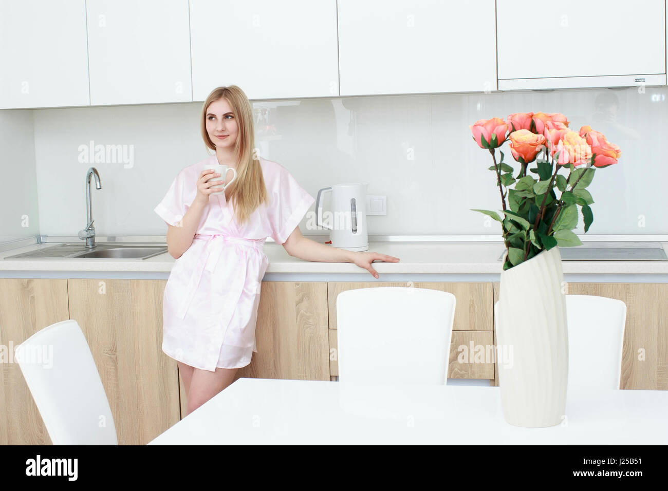 Donna sorridente in accappatoio in piedi con la tazza di caffè a casa in cucina Foto Stock
