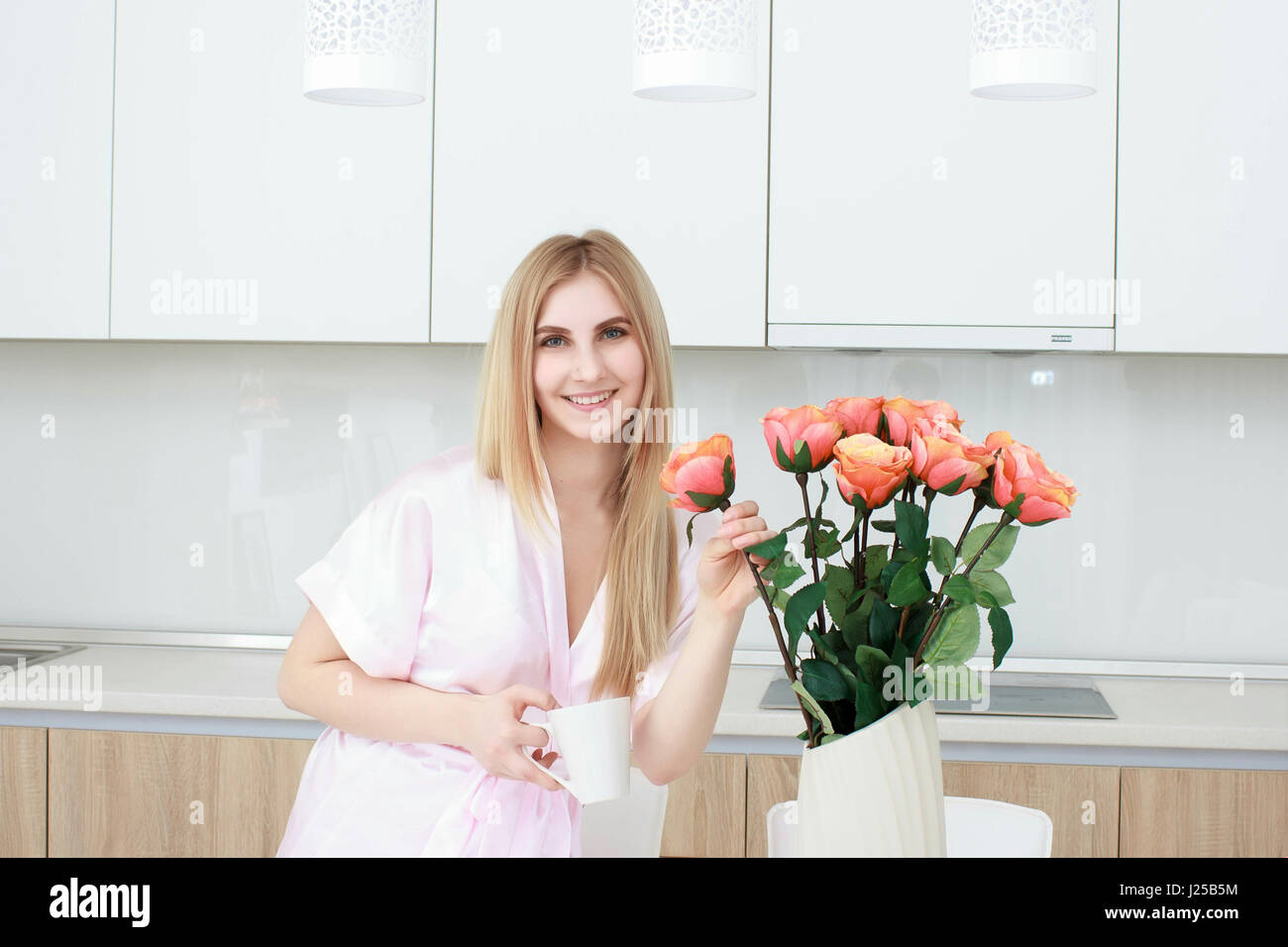 Donna sorridente in accappatoio in piedi con la tazza di caffè a casa in cucina Foto Stock