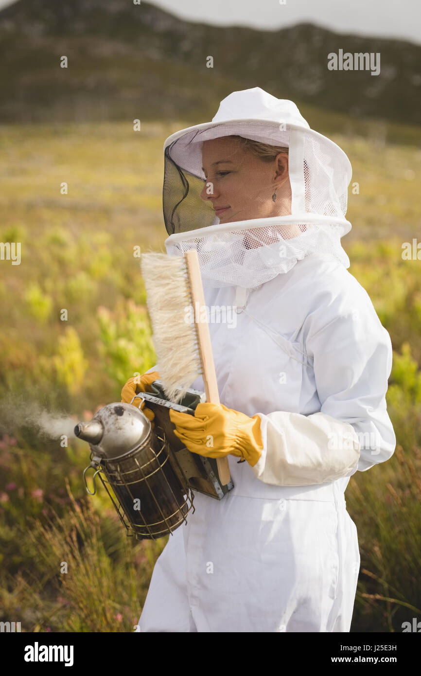 Apicoltore femmina holding bee fumatore e spazzola in agriturismo Foto Stock