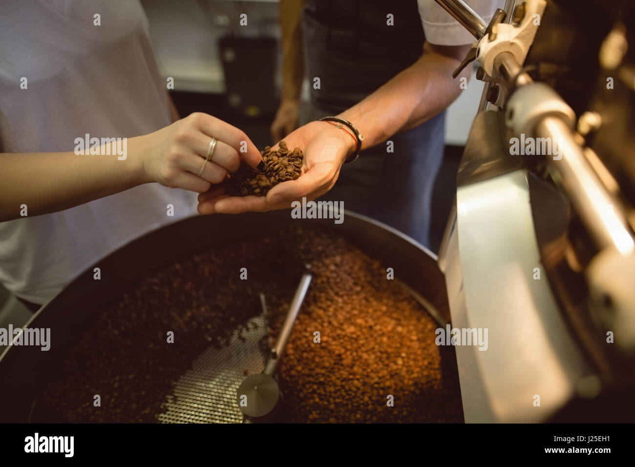 Maschio e femmina barista controllando i chicchi di caffè nella macchina di torrefazione in coffee shop Foto Stock