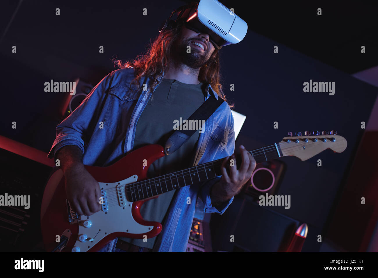 Maschio ingegnere audio utilizzando la realtà virtuale cuffie mentre suonando la chitarra in studio di registrazione Foto Stock