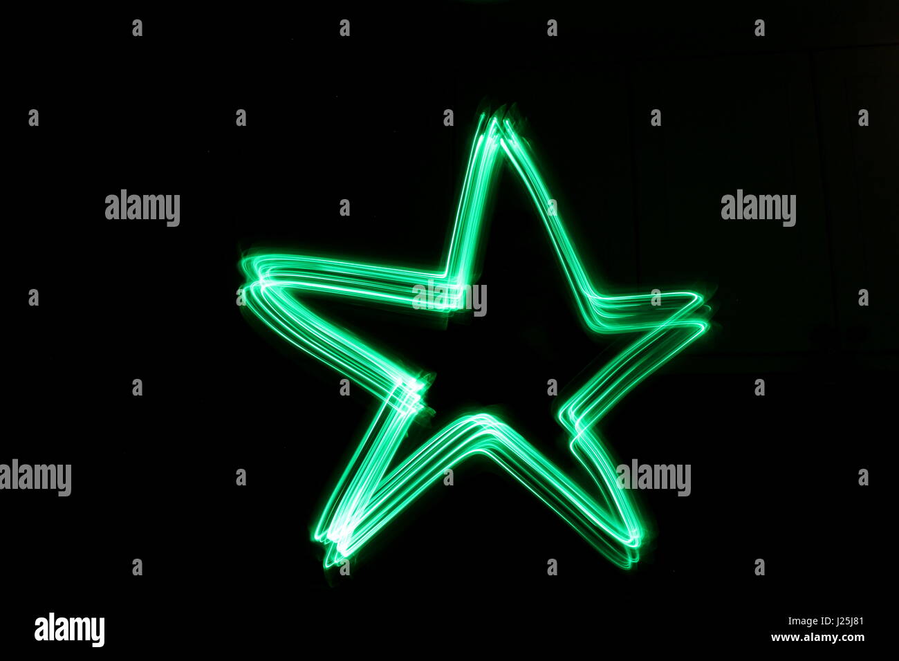 Una lunga esposizione fotografia di neon di colore verde in un astratto star forma del contorno su sfondo nero. Luce fotografia pittura, di colore in astratto Foto Stock