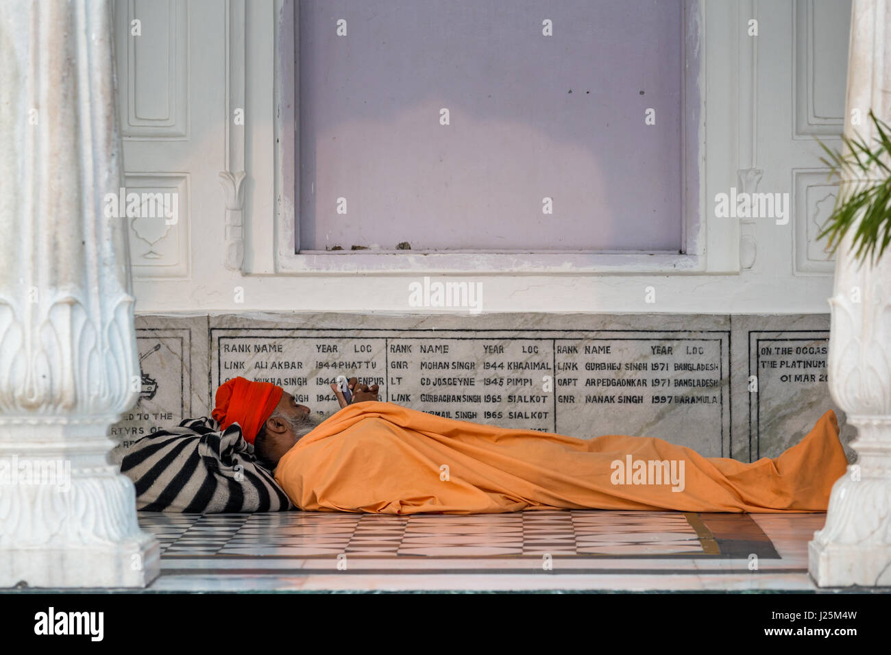 Un anziano pellegrino Sikh controllo sul suo cellulare durante il riposo presso il Tempio Dorato, Amritsar Punjab, India Foto Stock