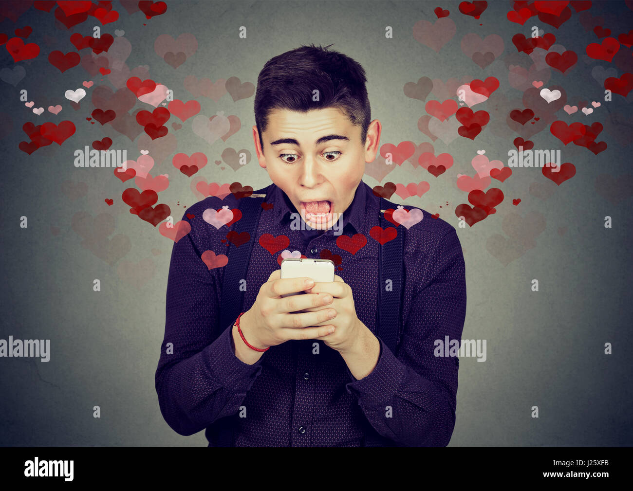 Ritratto giovane bello sconvolto l uomo invio ricevendo amore messaggio sms sul cellulare con cuori rossi volare lontano fino isolato sul muro grigio backg Foto Stock