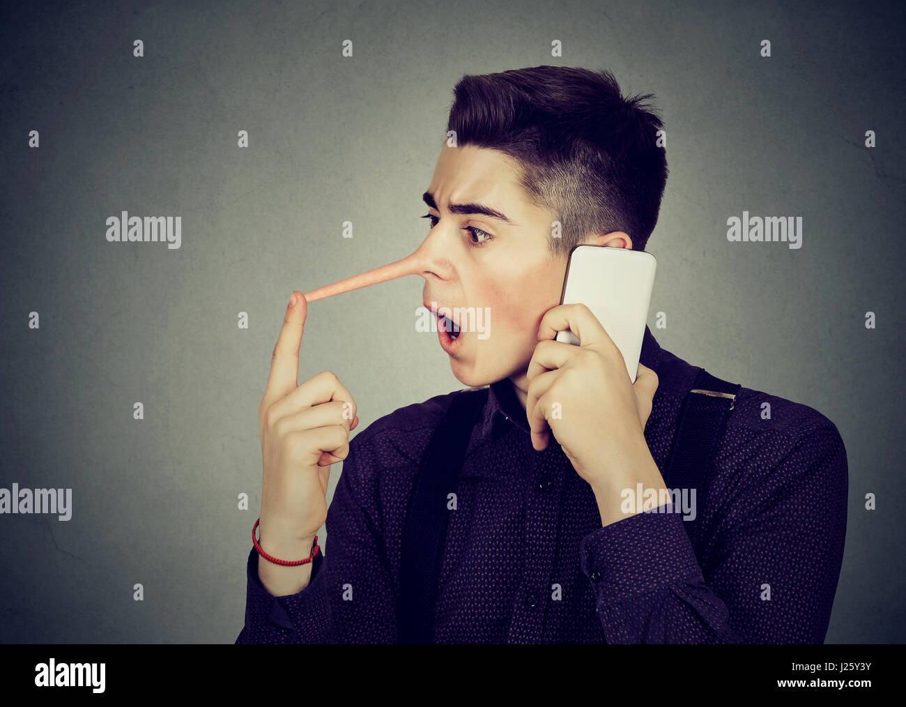 Sorpreso giovane con il naso lungo parlando al telefono cellulare isolata sul muro grigio Sfondo. Concetto bugiardo. Emozione umana sentimenti, tratti caratteriali Foto Stock