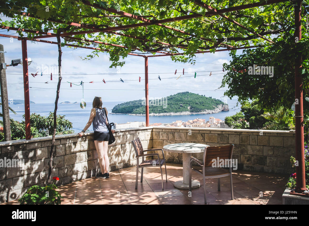 Giovane donna sul patio coperto affacciato su Dubrovnik con isola di Lokrum in distanza, Croazia Foto Stock