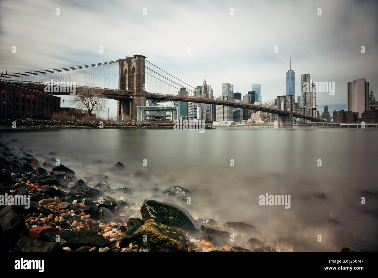 Spiaggia ghiaiosa con ponte di Brooklyn e downtown skyline di Manhattan a New York City Foto Stock