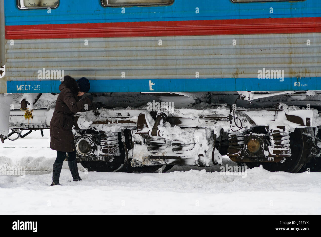 Provodnitsa femmina dipendente ferroviaria sgombero della neve dalle ruote del carrello ferroviario durante il periodo invernale in Russia Foto Stock