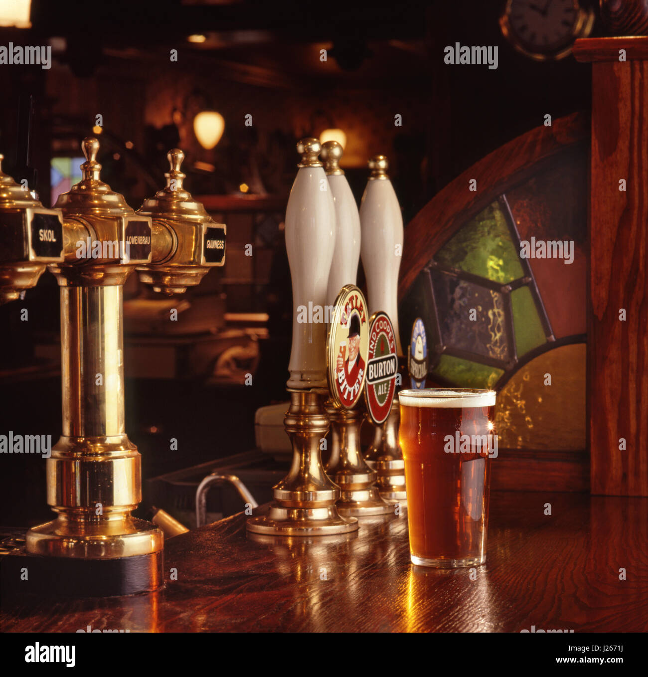Una pinta di birra servita su una superficie in legno del bar di una calda, tipica, tradizionale e invitante casa pubblica inglese, con birra e boccette di birra lager Foto Stock