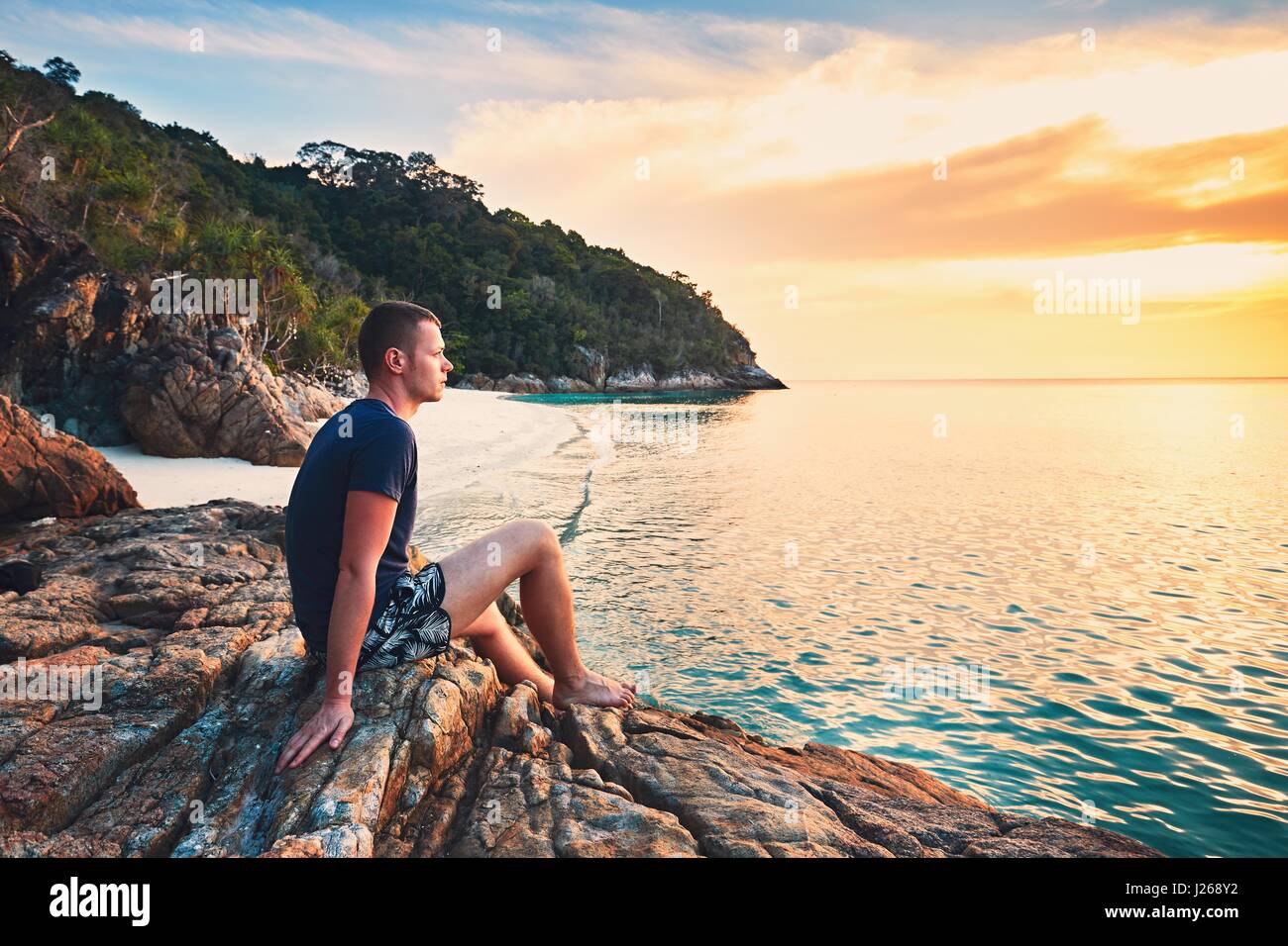 La contemplazione al tramonto. Da solo giovane uomo sulla bella spiaggia di sabbia. Foto Stock