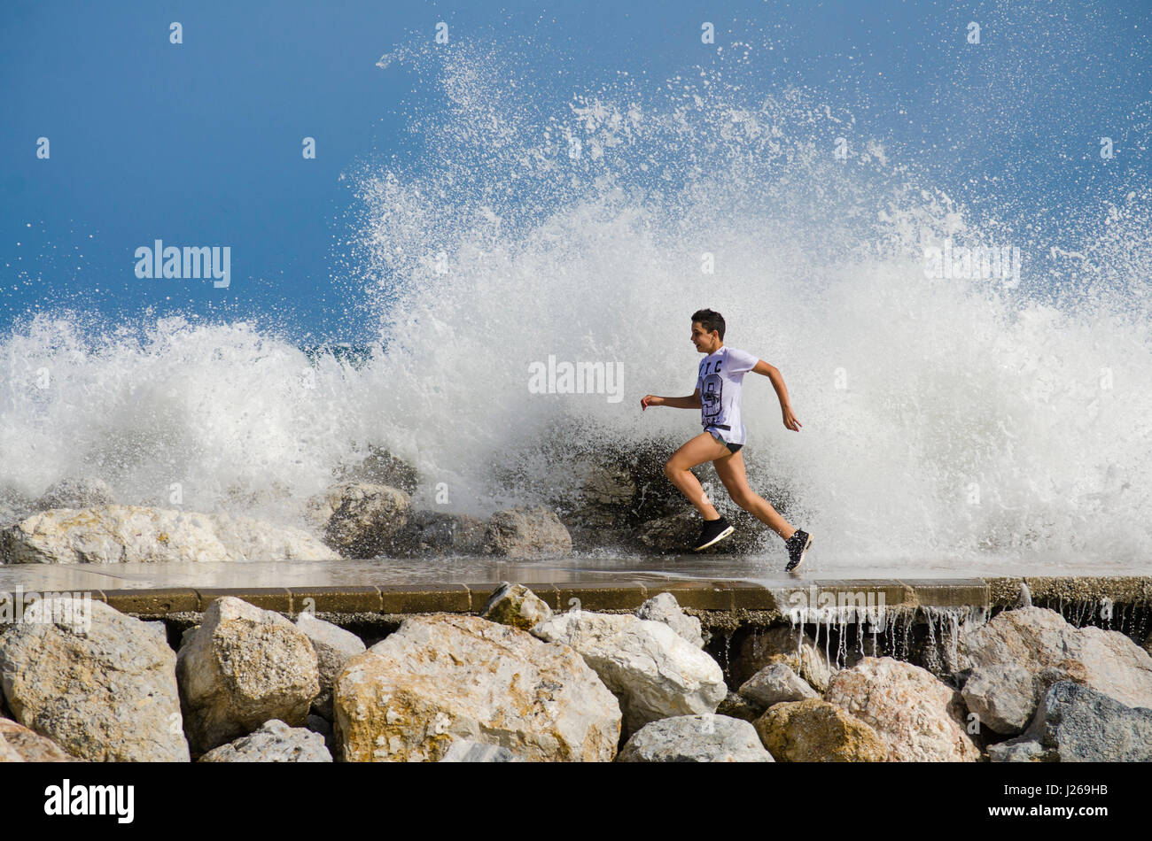 Ragazzo eccitato sul molo di scappare da spruzzi di acqua sul molo, giovane ragazzo adolescente adolescente,, Spagna. Foto Stock