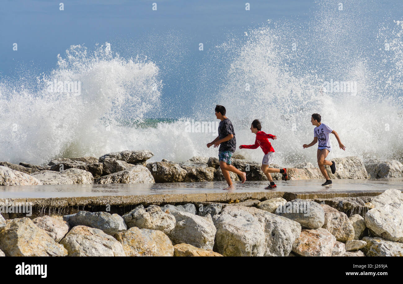Tre ragazzi eccitati sul molo di scappare da spruzzi di acqua sul molo, giovane ragazzo adolescente adolescente,, Spagna. Foto Stock